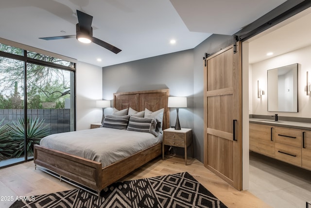 bedroom featuring sink, access to outside, expansive windows, a barn door, and light hardwood / wood-style floors