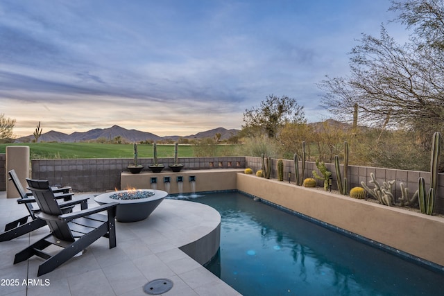 pool at dusk with an outdoor fire pit, a mountain view, and a patio area