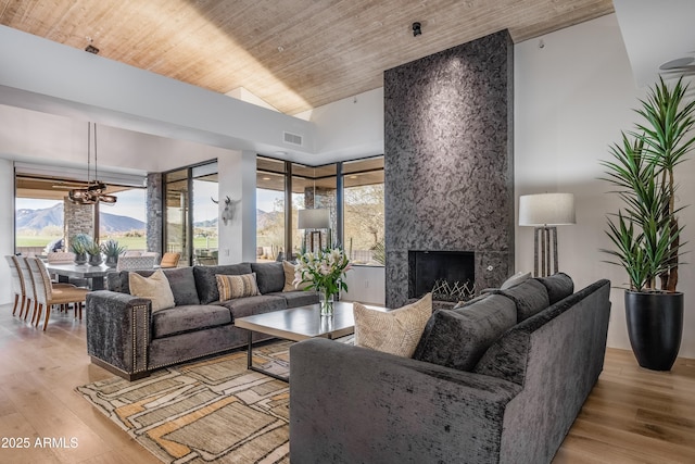 living room with wood ceiling, an inviting chandelier, a fireplace, light hardwood / wood-style floors, and a mountain view