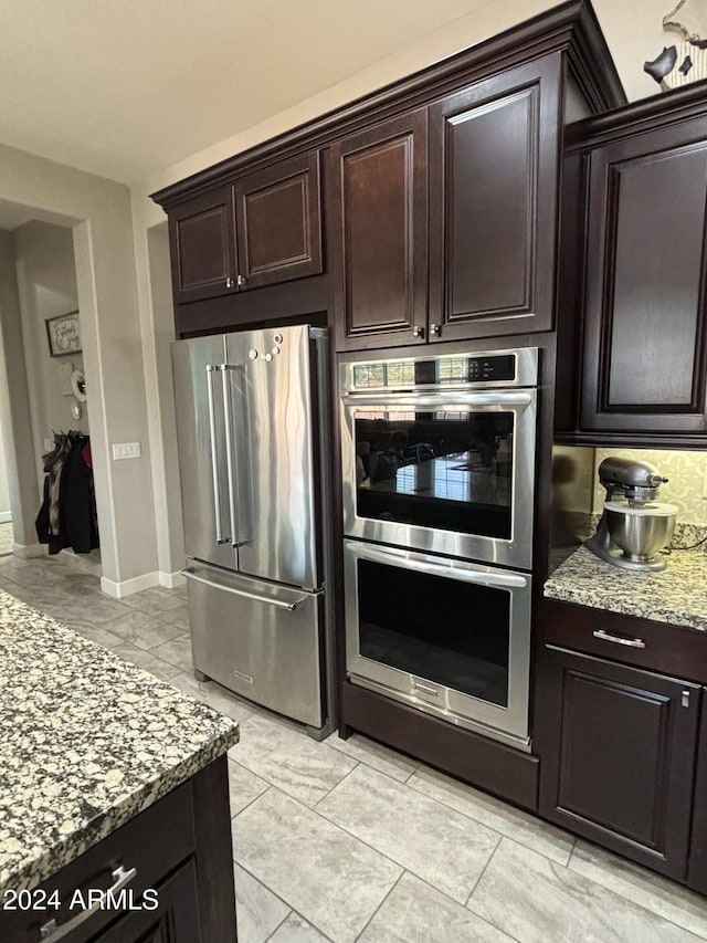 kitchen with dark brown cabinetry, light stone counters, and stainless steel appliances