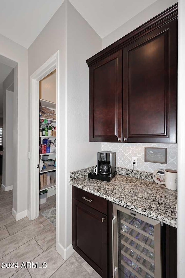 bar featuring tasteful backsplash, wine cooler, light stone countertops, and dark brown cabinets