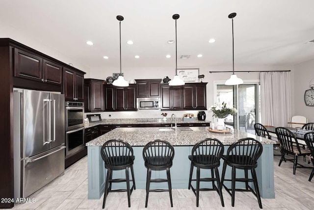 kitchen with sink, decorative light fixtures, a kitchen island with sink, a breakfast bar, and appliances with stainless steel finishes