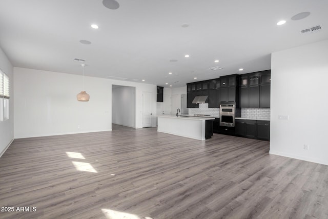 kitchen featuring sink, double oven, backsplash, hardwood / wood-style floors, and an island with sink