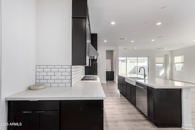 kitchen with sink, decorative backsplash, stainless steel appliances, a center island with sink, and light wood-type flooring