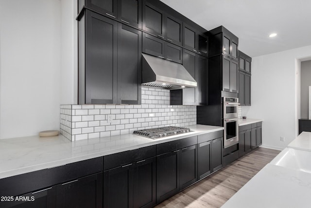 kitchen with appliances with stainless steel finishes, light stone countertops, light hardwood / wood-style floors, and backsplash