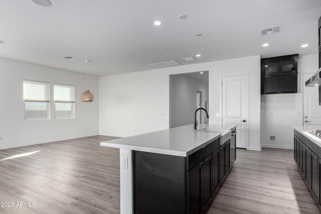 kitchen with sink, hanging light fixtures, an island with sink, and light wood-type flooring