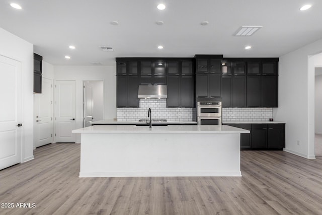 kitchen with tasteful backsplash, light hardwood / wood-style floors, and an island with sink