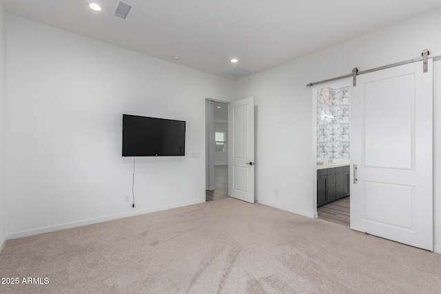 unfurnished bedroom with a barn door, light carpet, and ensuite bath