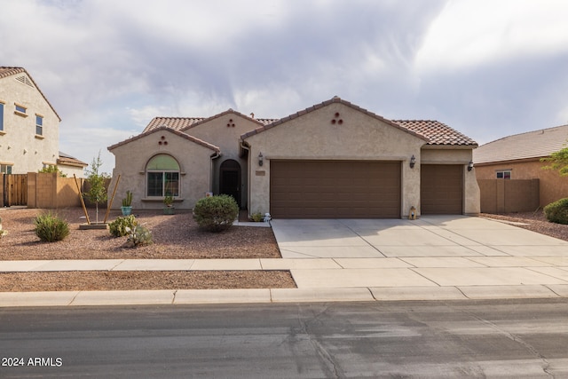 mediterranean / spanish-style house featuring an attached garage, a tiled roof, fence, and stucco siding