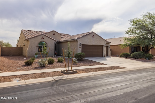 mediterranean / spanish house with driveway, a garage, a tiled roof, fence, and stucco siding