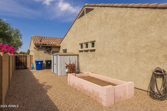 exterior space featuring a storage shed, an outdoor structure, fence, a garden, and a gate