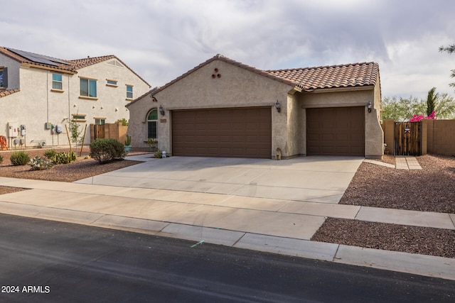 mediterranean / spanish-style home featuring stucco siding, an attached garage, a gate, driveway, and a tiled roof