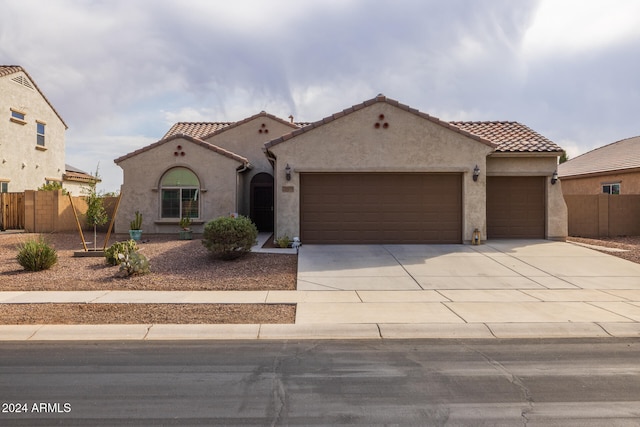 mediterranean / spanish home featuring a garage, a tile roof, fence, concrete driveway, and stucco siding