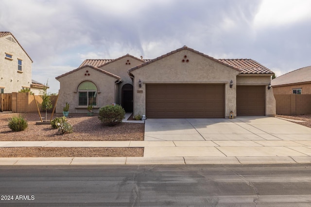 mediterranean / spanish-style house with an attached garage, fence, a tile roof, concrete driveway, and stucco siding