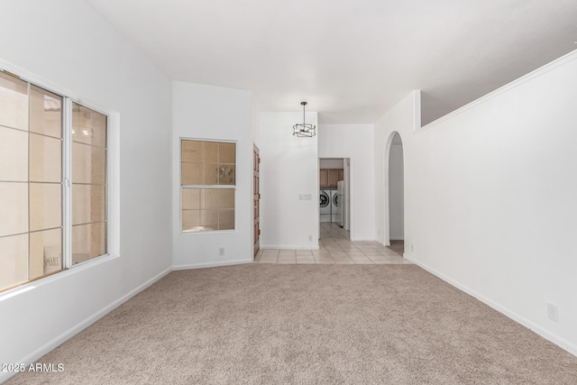 empty room featuring light colored carpet, washing machine and dryer, and a notable chandelier