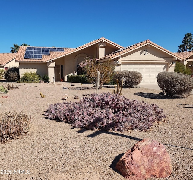 mediterranean / spanish-style house with an attached garage, a tile roof, solar panels, and stucco siding