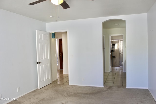 unfurnished room with arched walkways, carpet flooring, a ceiling fan, and baseboards