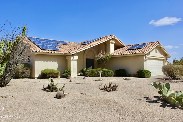 mediterranean / spanish-style home featuring a garage, a tiled roof, roof mounted solar panels, and stucco siding