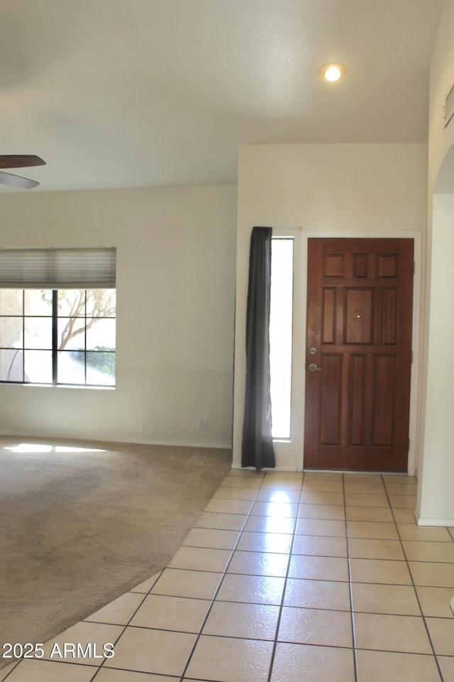 entryway featuring a ceiling fan, a healthy amount of sunlight, light carpet, and light tile patterned floors