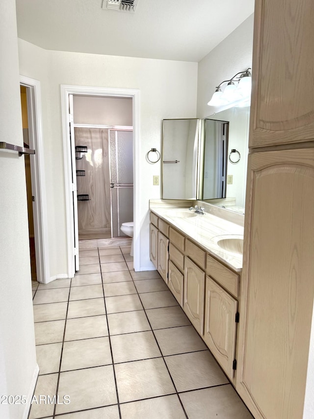 bathroom featuring a shower with door, double vanity, toilet, a sink, and tile patterned flooring