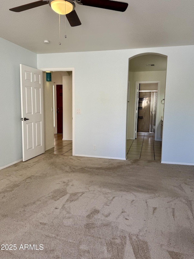 spare room featuring carpet floors, ceiling fan, visible vents, and arched walkways