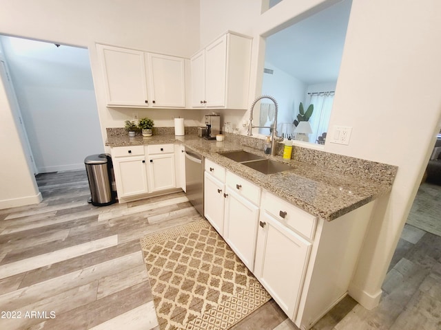 kitchen with a sink, white cabinetry, light wood-style floors, light stone countertops, and dishwasher