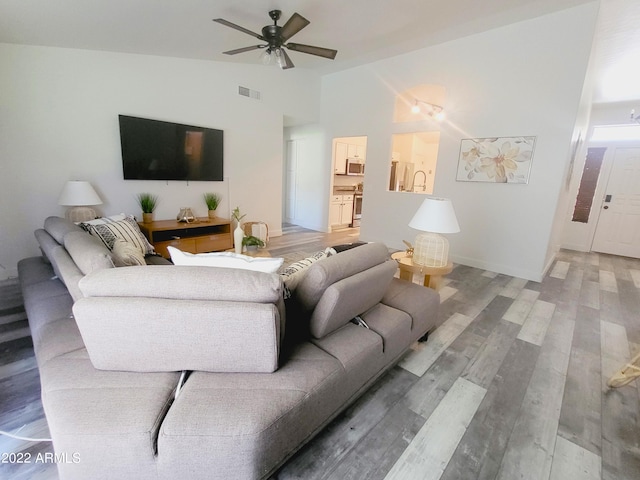 living room with light wood finished floors, baseboards, visible vents, a ceiling fan, and high vaulted ceiling