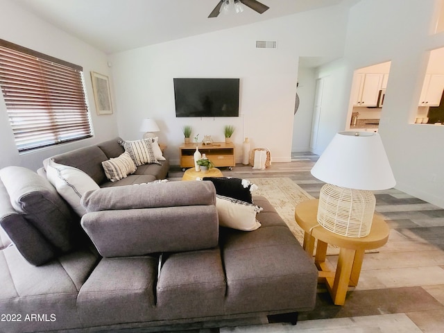 living area with light wood-type flooring, lofted ceiling, visible vents, and ceiling fan