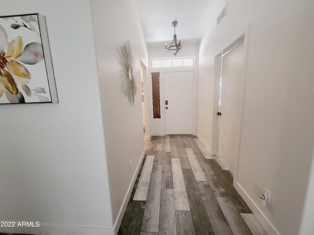 hallway with an inviting chandelier, baseboards, visible vents, and dark wood-style flooring