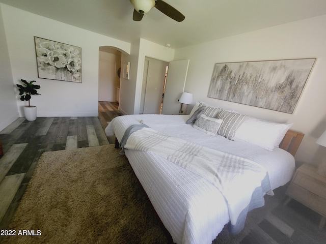 bedroom with a ceiling fan, arched walkways, and wood finished floors