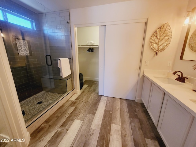 full bath featuring wood finished floors, a sink, double vanity, a stall shower, and a walk in closet