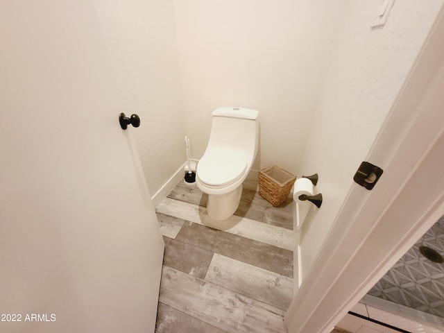 bathroom with toilet, baseboards, and wood finished floors