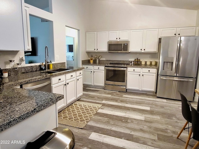 kitchen featuring light wood finished floors, appliances with stainless steel finishes, a sink, and white cabinets