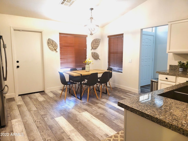 dining area with an inviting chandelier, light wood-style flooring, visible vents, and vaulted ceiling