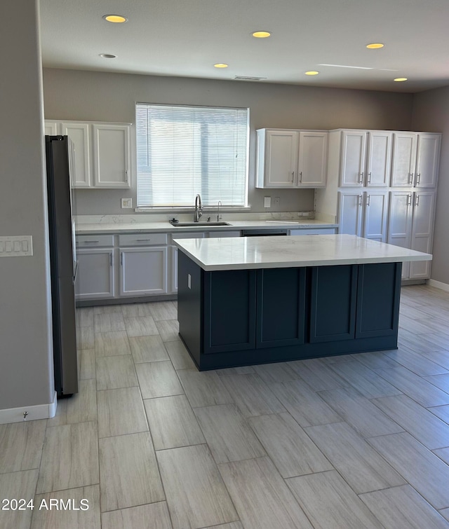 kitchen with stainless steel fridge, a center island, white cabinets, and sink