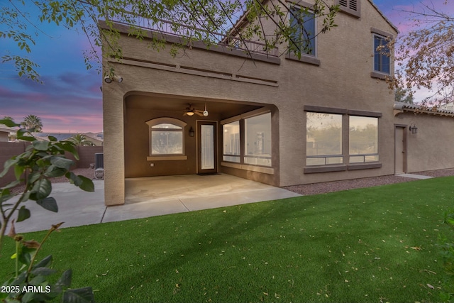 rear view of house with a patio area, a lawn, and stucco siding