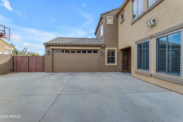 view of home's exterior with stucco siding, concrete driveway, an attached garage, fence, and a tiled roof