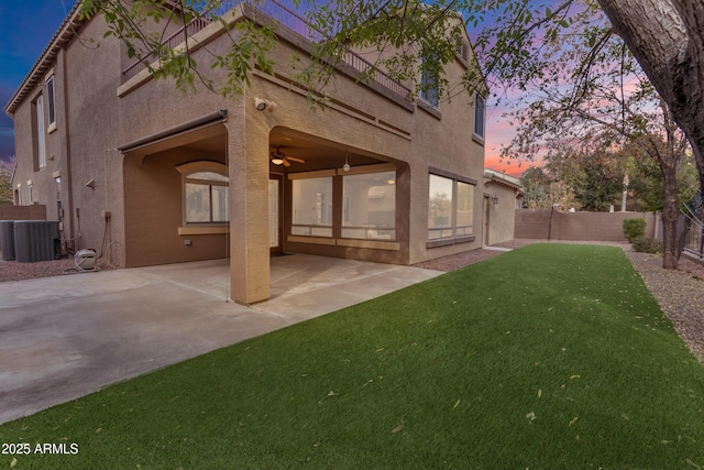 back of property at dusk featuring a patio, a fenced backyard, ceiling fan, a yard, and stucco siding