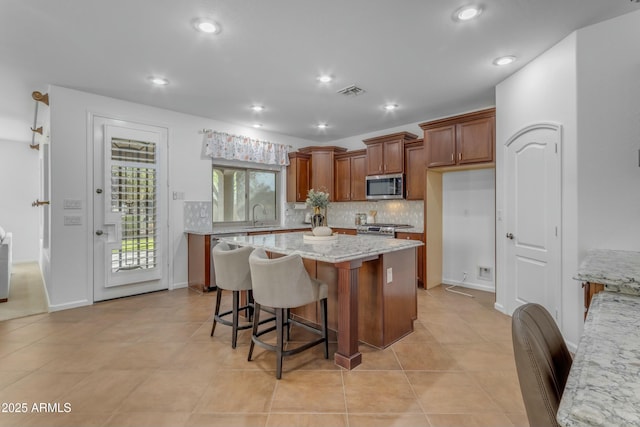 kitchen with a center island, stainless steel appliances, visible vents, decorative backsplash, and a sink