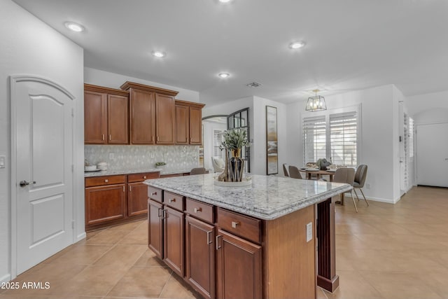 kitchen with light tile patterned flooring, a kitchen island, visible vents, backsplash, and light stone countertops