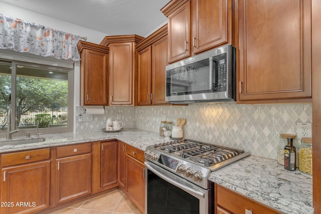 kitchen with light tile patterned flooring, a sink, appliances with stainless steel finishes, backsplash, and light stone countertops