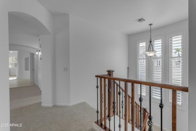 corridor with an upstairs landing, arched walkways, visible vents, and carpet flooring