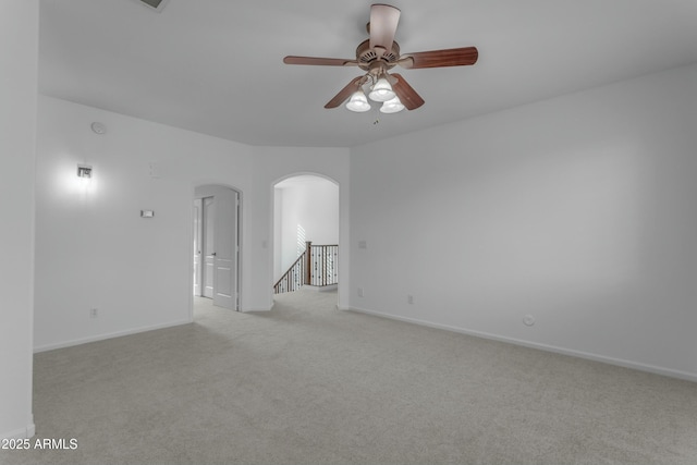 spare room with baseboards, arched walkways, ceiling fan, and light colored carpet