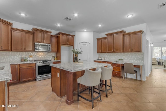 kitchen featuring light tile patterned flooring, stainless steel appliances, visible vents, light stone countertops, and brown cabinetry