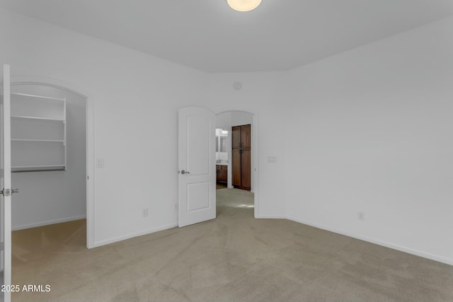 unfurnished bedroom featuring arched walkways, a walk in closet, carpet flooring, and baseboards