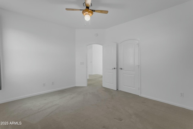 carpeted spare room with ceiling fan, arched walkways, and baseboards