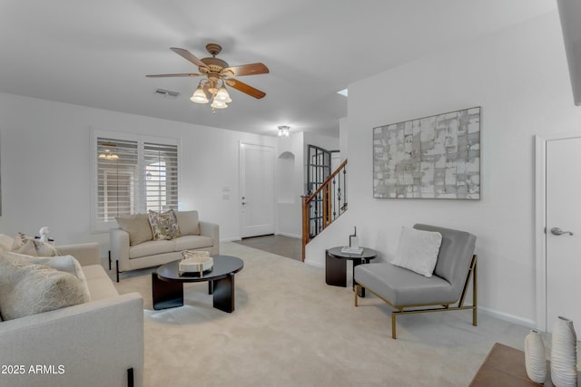 carpeted living room featuring stairs, baseboards, visible vents, and a ceiling fan