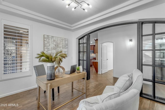 home office featuring arched walkways, a raised ceiling, wood finished floors, and baseboards