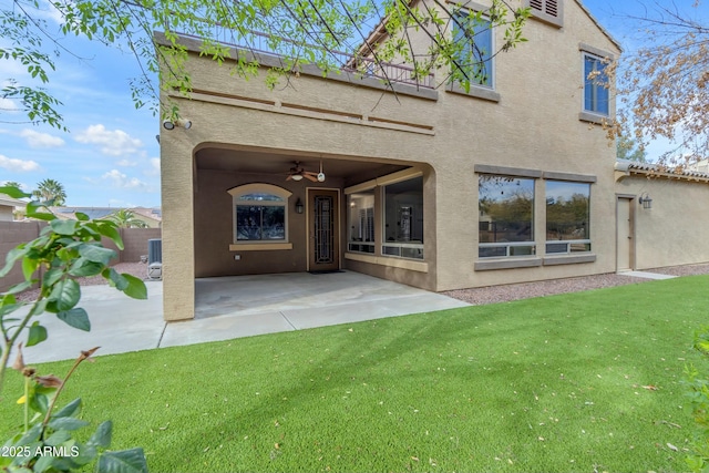 rear view of house featuring stucco siding, a lawn, a patio area, ceiling fan, and fence