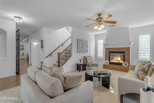 living room featuring a fireplace, a ceiling fan, visible vents, baseboards, and stairway